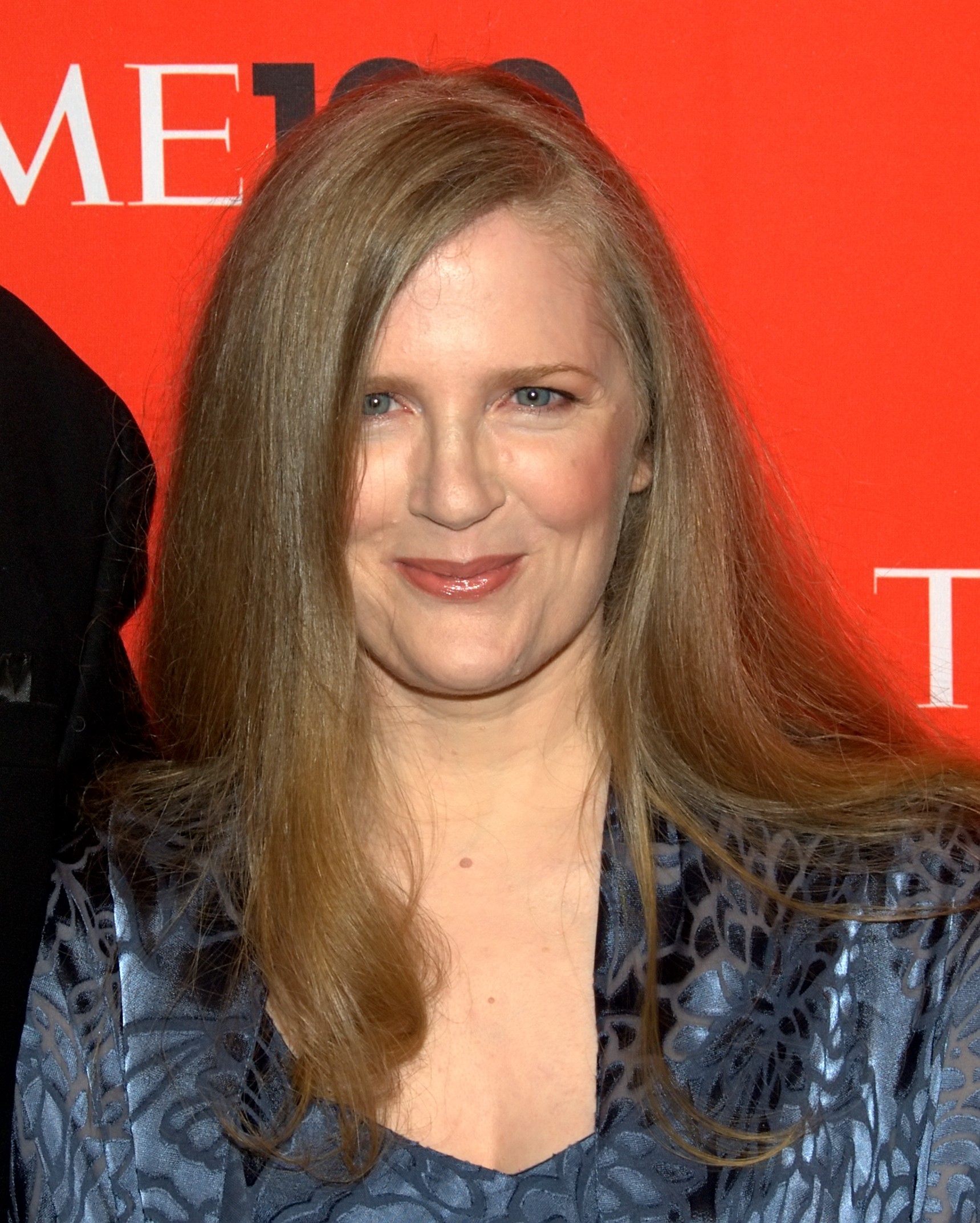 Suzanne Collins in 2010, smiling in front of a red Time 100 event backdrop.