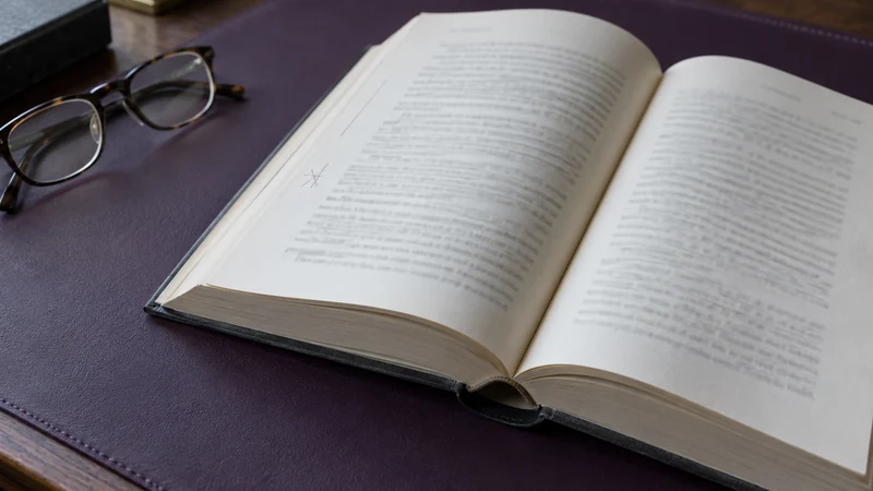 An open used book with intact pages and light pencil marks beside reading glasses.