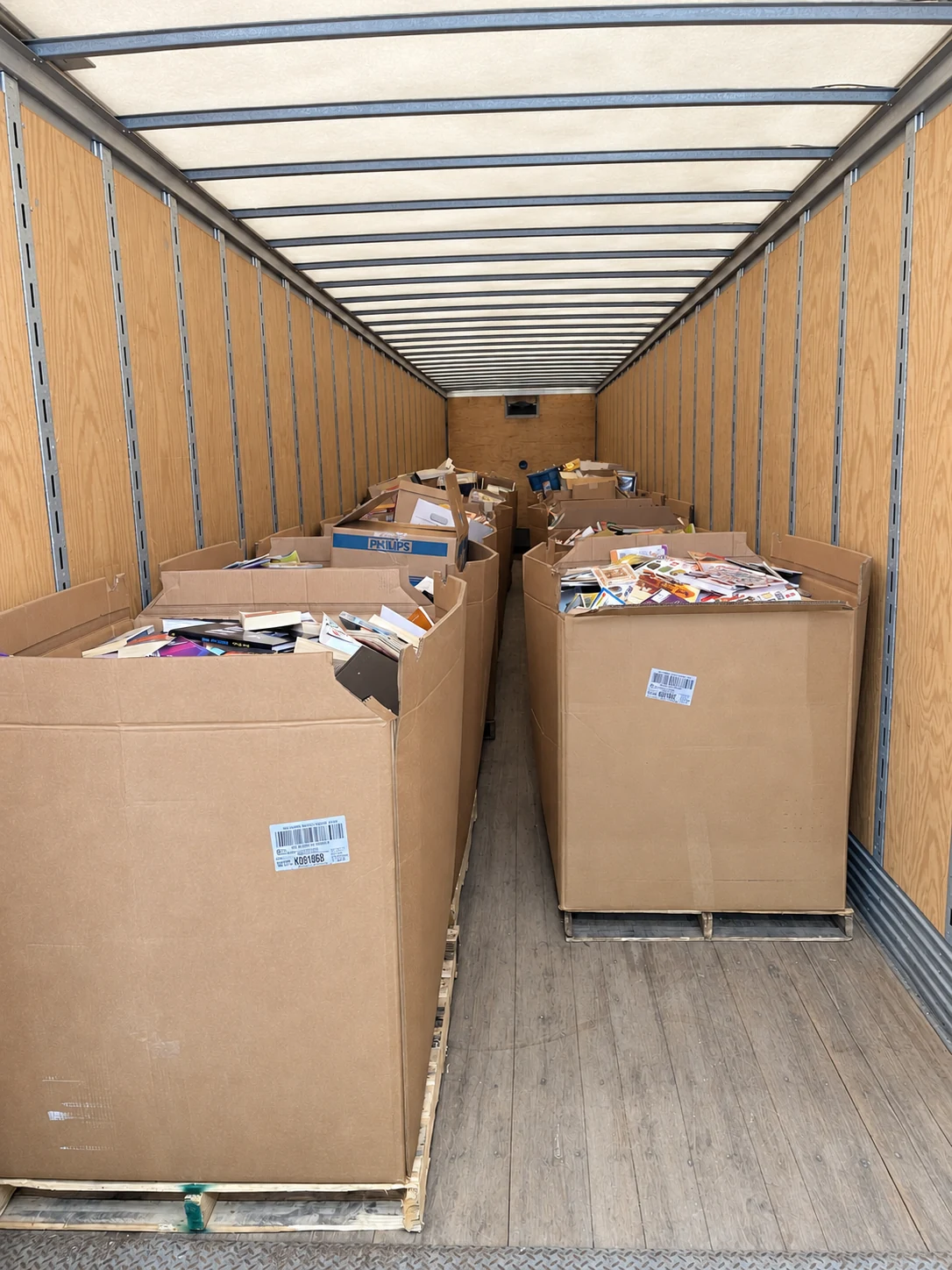 Large Gaylord boxes filled with books on pallets inside a trailer.