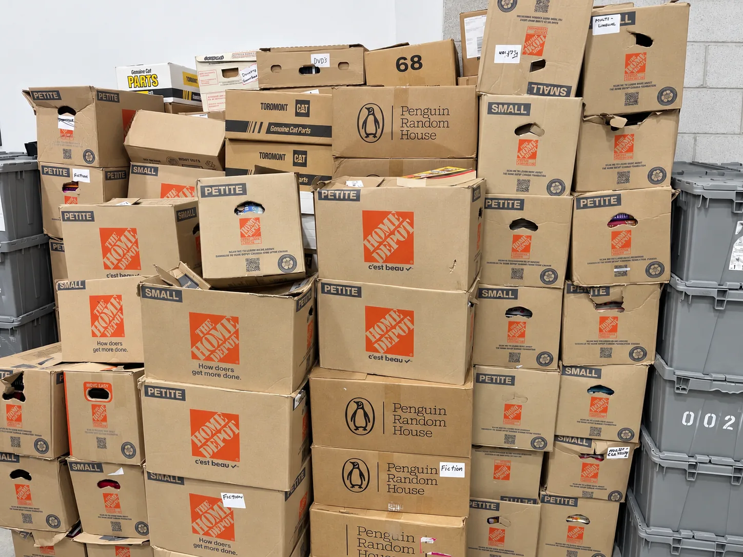 Reused cardboard boxes stacked with books beside gray collection bins.